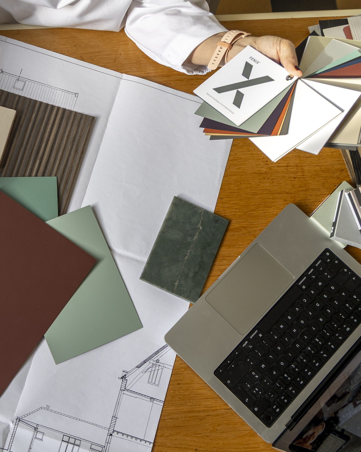 Materiaalstalen en een laptop op uitgespreide bouwplannen
