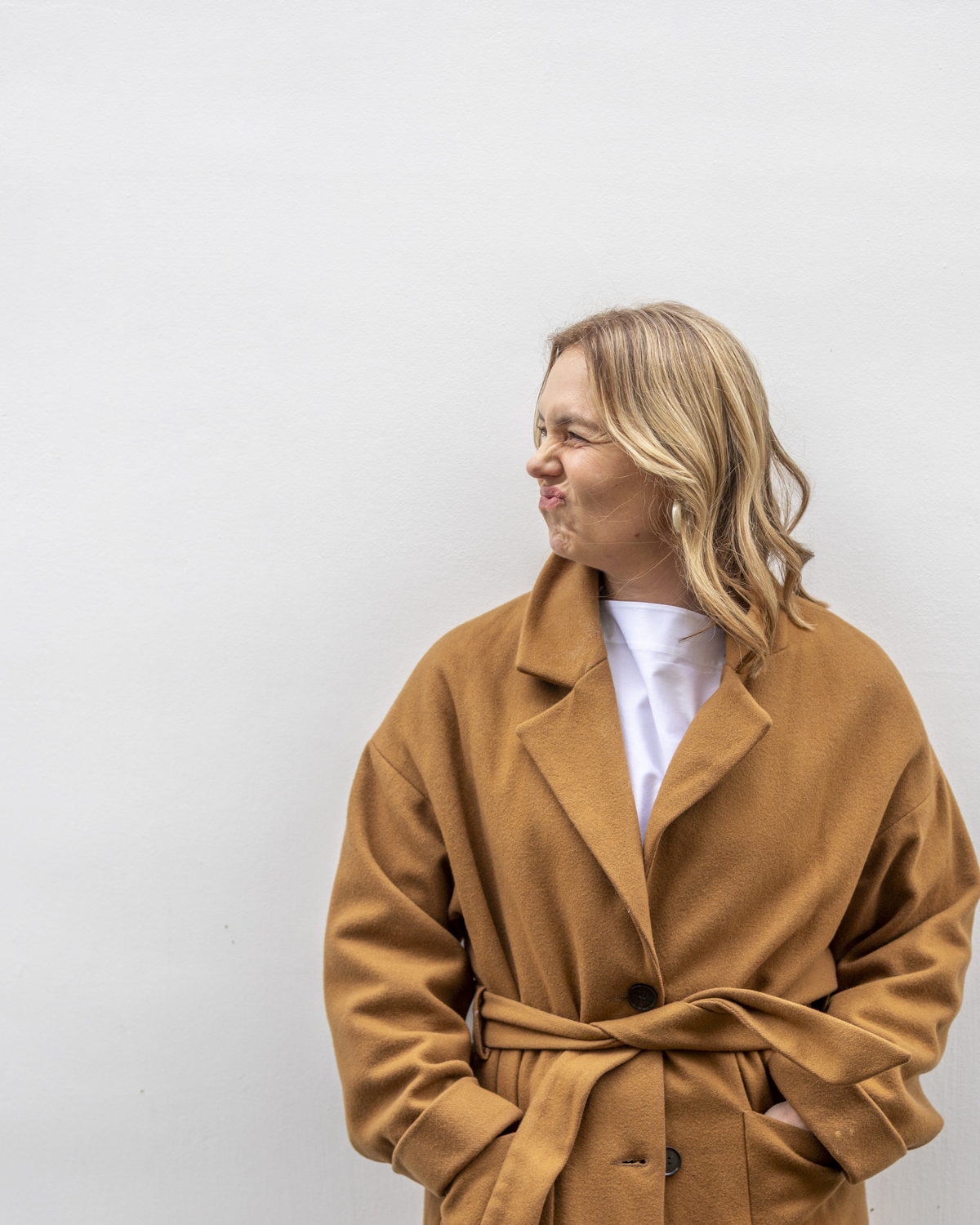 Barbara in een camel mantel tegen een witte muur